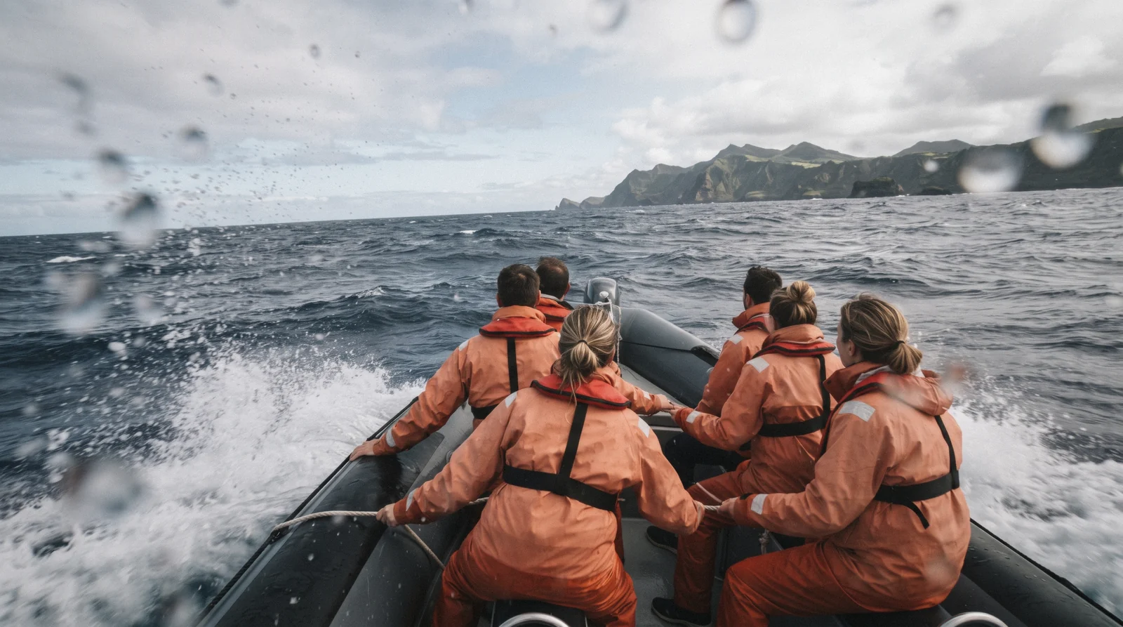 A small group of travellers in waterproofs watching for whales from the bow of a boat in open Atlantic water
