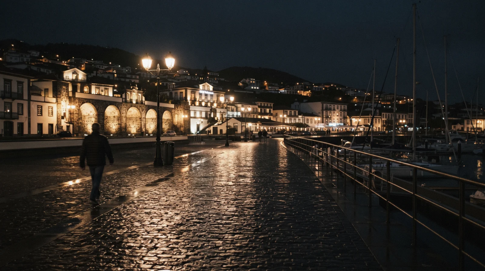 The marina promenade of Ponta Delgada at dusk, street lamps lit along the waterfront with the town lights coming on behind