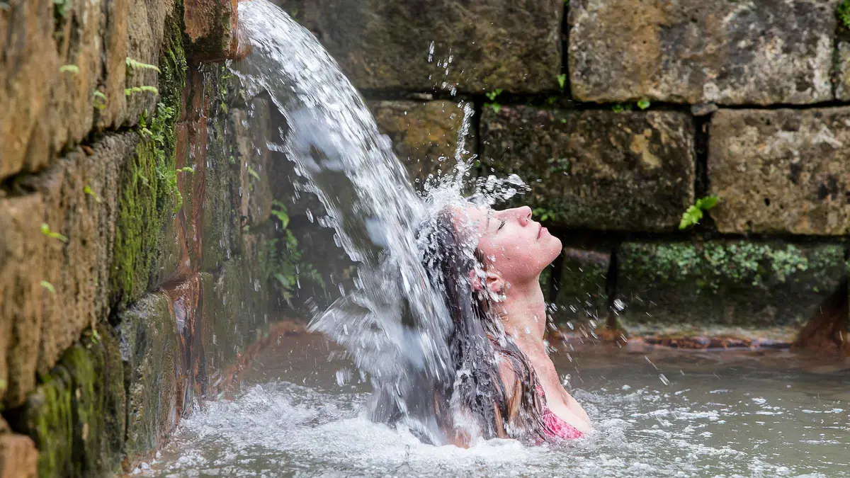A bather under the small waterfall at the Poca da Dona Beija hot springs in Furnas