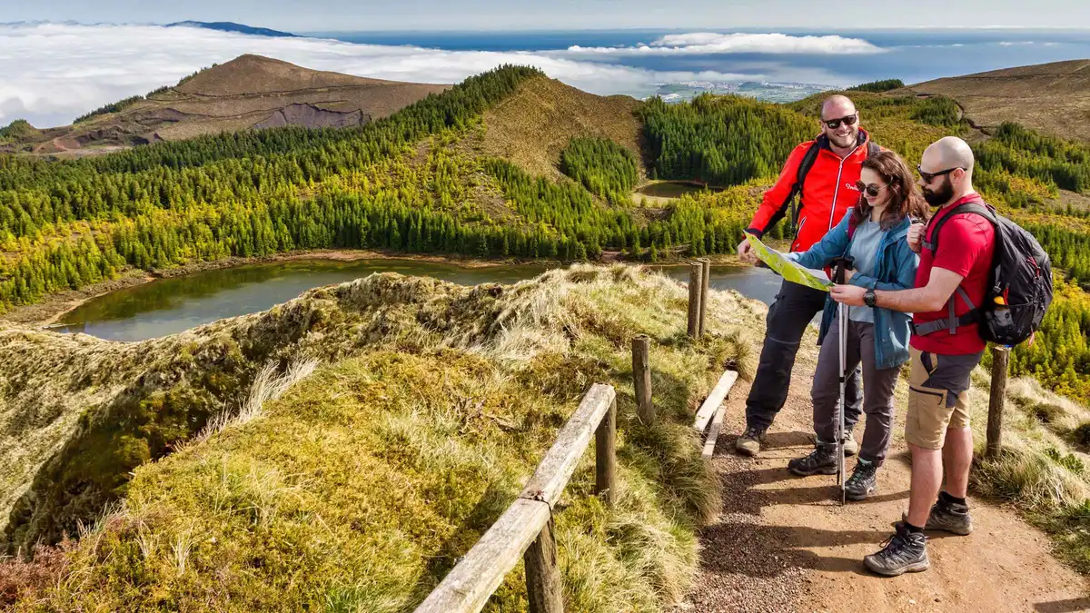 A guide briefing two hikers in red jackets on the trail above a Sete Cidades lake