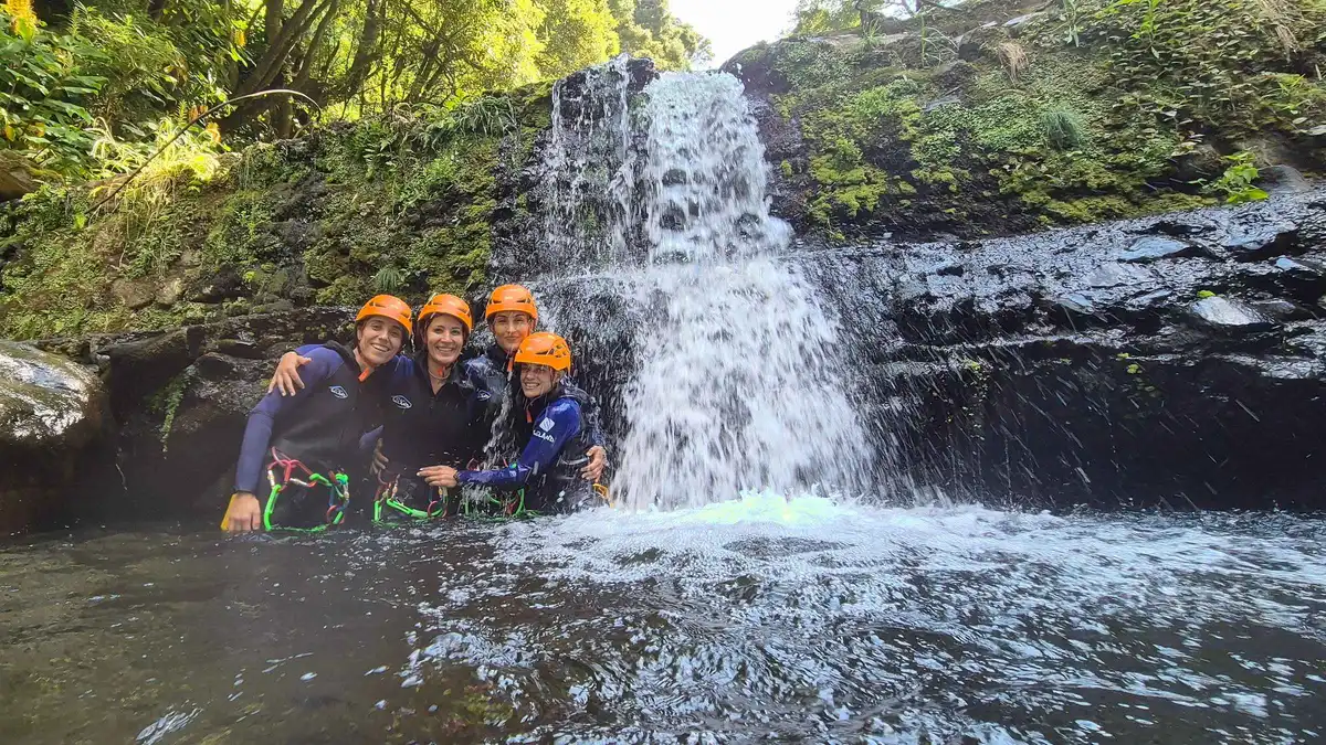 Canyoneers in helmets posing in the plunge pool below a waterfall at Salto do Cabrito, Azores