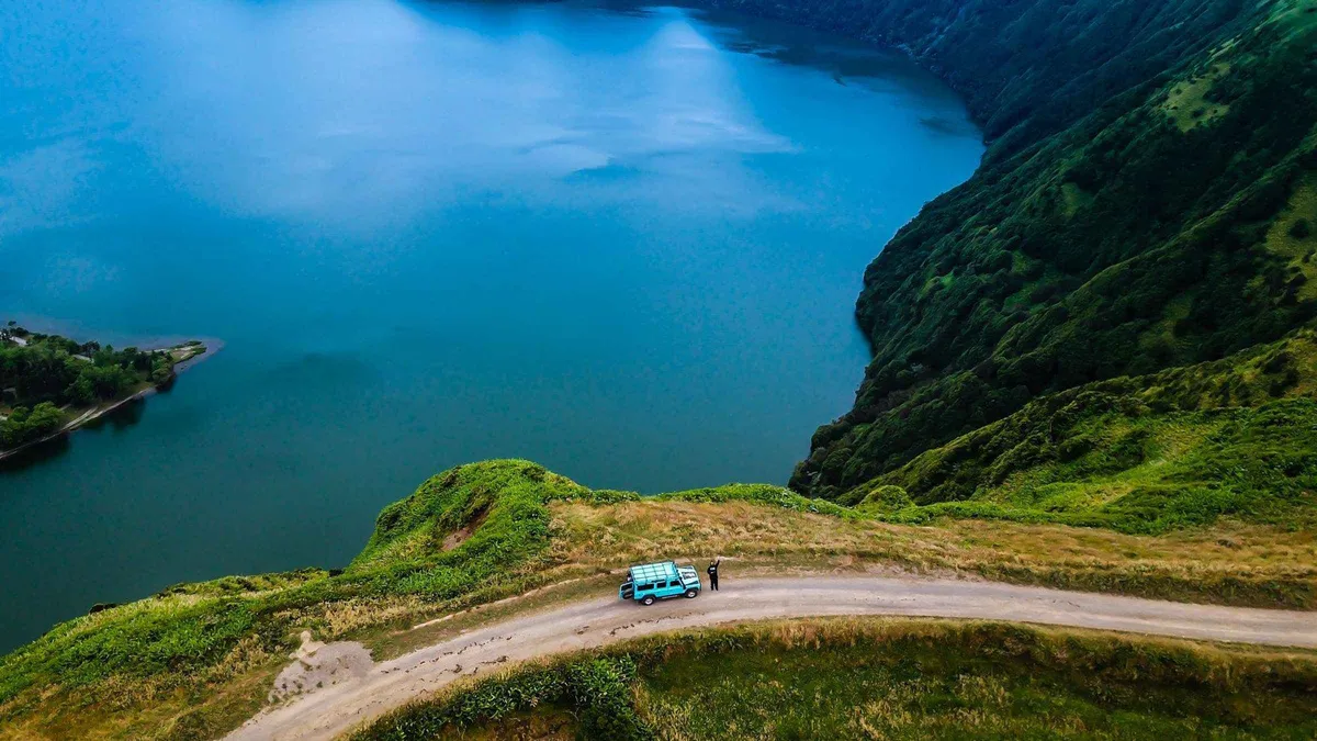 A lone car on the rim road above the deep blue crater lake at Sete Cidades on a half-day Azores jeep tour