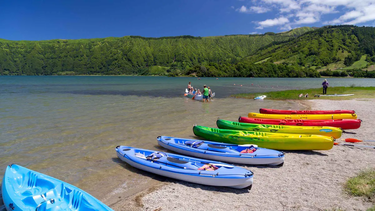 A row of brightly colored kayaks on the shore of the Blue Lake at Sete Cidades