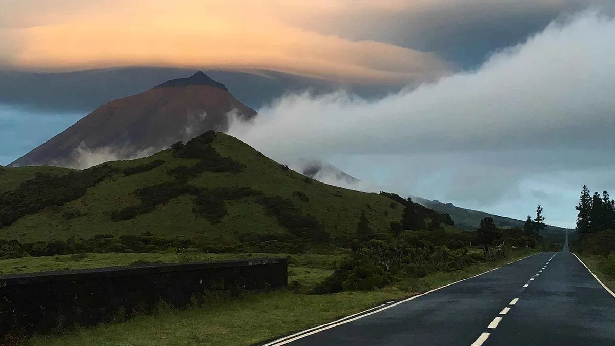 An empty road running toward Mount Pico under a lenticular cloud on Pico island