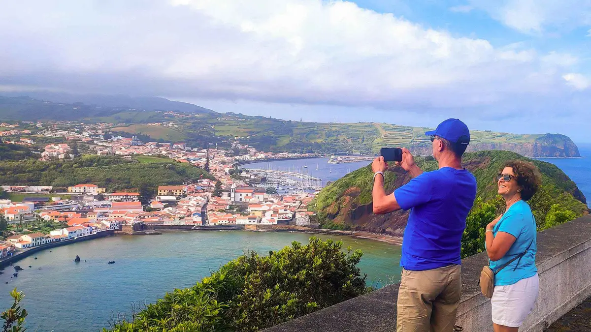 Two travelers photographing the bay and hillside town of Horta on Faial island from a viewpoint
