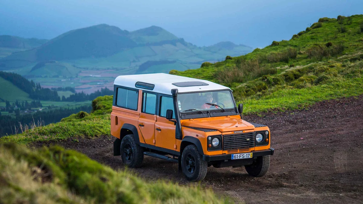 An orange 4x4 jeep on a dirt track in the green hills of the Sete Cidades interior