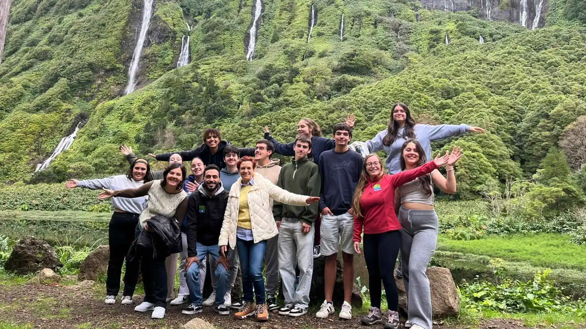 A tour group posing in front of waterfall-streaked green cliffs on Flores island