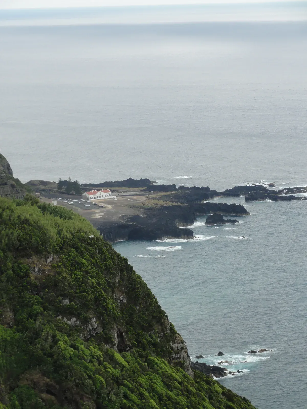 The Ponta da Ferraria point seen from the clifftop: the spa building with its red roof, the lava ledge and the natural pool where hot springs meet the Atlantic