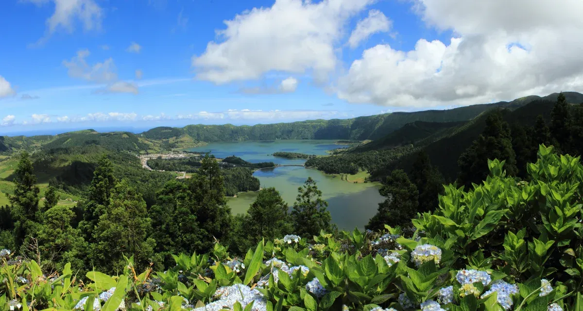 The green and blue twin lakes of Sete Cidades seen from the crater rim, with the village and the bridge below